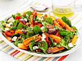 A colourful plate of salad with roasted carrots, dried tomatoes, red peppers, sheep's cheese, spinach, herbs and nuts