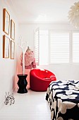 Red upholstered armchair next to stylised tree used as clothes rack in corner of white bedroom with white interior window shutters