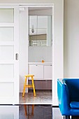 Armchair with blue cover in front of doorway with open sliding door and view of yellow stool in front of washstand