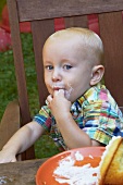 Kleiner Junge sitzt am Gartentisch & schleckt Finger ab