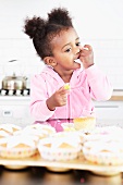 A little girl eating frosting from cupcakes