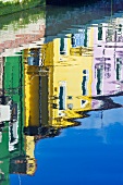 Historische Häuser in verschiedenen Farben spiegeln sich auf der Wasseroberfläche eines Kanals