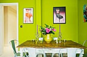 Candlestick and bouquet on antique table below modern, framed posters on green wall