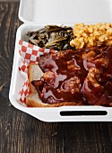 Barbecue Snout Sandwich on White Bead with Collard Greens and Macaroni and Cheese in a Styrofoam Container