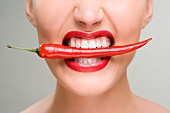 Junge Frau hält eine rote Chilischote zwischen den Zähnen