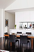 Wooden dining table and black chairs in front of white fitted kitchen with sink unit