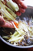 Hands adding julienned vegetables to a pot of hot water