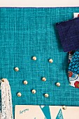 Drawing pins and fabric swatches pinned on turquoise linen fabric