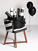 Rolls of paper in basket on chair with wooden frame and black and white cover next to black balloons on metal frames