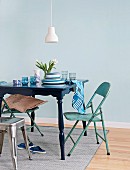 Colour-coordinated accessories on table painted dark blue, turquoise folding chairs and vintage-style industrial metal stool