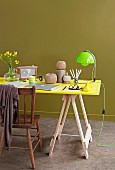 Arbeitsplatz mit Vintage Stuhl zu leuchtend gelber Tischplatte auf Böcken und neongrüner Leuchte, abgerundet durch olivegrünen Hintergrund