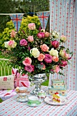Romantic table setting in the garden with a gorgeous bouquet of roses in a silver chalice from an English tea service and floral table cloth