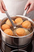 Doughnuts being fried in a pan and being removed with a slotted spoon