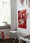 Teenage girl's bedroom with various utensils in containers on red organiser board above laptop on white folding table and metal, upholstered chair in front of window with white curtain
