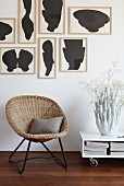 Vintage basket chair below artworks by Fons Haagmans and next to low table on castors with coral-shaped vase