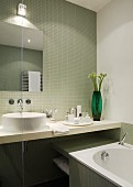 View of washstand and bathtub in bathroom with pistachio green mosaic tiles