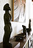 Wooden African sculpture on sideboard-style shelving unit below picture on wall