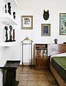 Wooden stool below shelves of African sculptures opposite partially visible bed in corner of bedroom