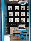 View through open door of blue dining table and chairs in front of black-painted wall with teapots displayed in square niches