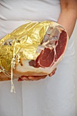 A woman holding a Parma ham wrapped in gold foil