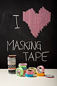 Colourful masking tape rolls in front of blackboard with heart motif and lettering