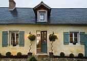 Einfaches, nordfranzösisches Landhaus mit Schieferdach, spitzer Dachgaube und eleganter Pflanzendekoration neben der Eingangstür