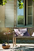Scatter cushions on wooden bench, delicate bistro table and bouquet of lavender in basket in front of window of Provençal country house