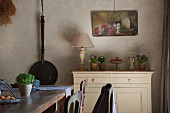 Provençal dining room with cast iron pan and still-life painting on wall; flower arrangements on simple cabinet and rustic wooden table