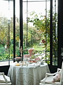 Lit candles in candelabra on set table in conservatory with view into late-summer garden