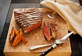 Partially Sliced Steak on a Cutting Board with Sweet Potato Fries; Wine Glass