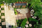View down onto precise garden with stone-floored seating area, rows of flower pots and beds between stone flags