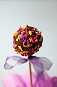 A cake pop decorated with dinosaur sprinkles