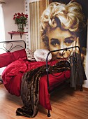 Black metal bed with claret bed linen and fur blanket; large portrait of Marilyn Monroe on wall