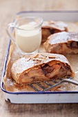 Three slices of pear and quince strudel and a jug of cream on a baking tray