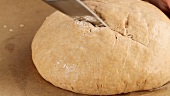 A loaf of bread being brushed with water, scored and sprinkled with sunflower seeds (close-up)