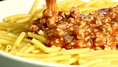 Minced meat sauce being poured over macaroni