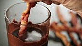 A fried bacon skewer being dipped in chocolate sauce
