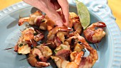 A plate of prawns wrapped in bacon with a hand reaching for one