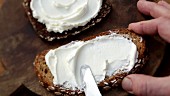 Cream cheese being spread on a slice of wholemeal bread