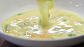Cremige Gemüsesuppe in einen Teller geben (Close Up)