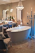 Kerzenstimmung in modernem Badezimmer mit freistehender Badewanne und barocken Elementen; neben der Badewanne ein silberner Standkerzenleuchter