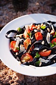 Squid Ink Pasta with Cherry Tomatoes, Pine Nuts and Parmesan Cheese in a White Bowl
