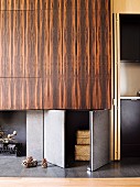 Fitted cupboards with grey doors and doors veneered in African wood next to open-plan kitchen