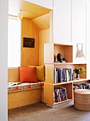 Wood-clad window niche with seat cushion and scatter cushions on built-in window seat next to fitted cupboards with shelving units