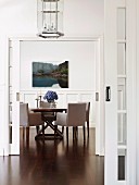 Einblick in elegantes hohes Esszimmer mit Holztisch und gepolsterten Stühlen, an der weißen Wand eine Landschaftsaufnahme