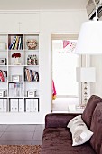 White built-in shelf with square compartments; in front of it a plush, brown sofa