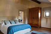 Double bed with blue and white bed linen and rustic wooden wardrobe within historical walls of Proven