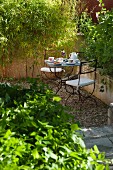 Secluded seating area in Mediterranean garden with wrought iron chairs and table set for two for afternoon coffee