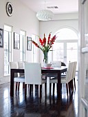 Red gladioli on large dining table and chairs with leather upholstery in classic black and white dining room
