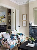 Polstersessel mit fröhlich floralem Bezug in klassischem Wohnraum mit Stuckdecke und offenem Kamin